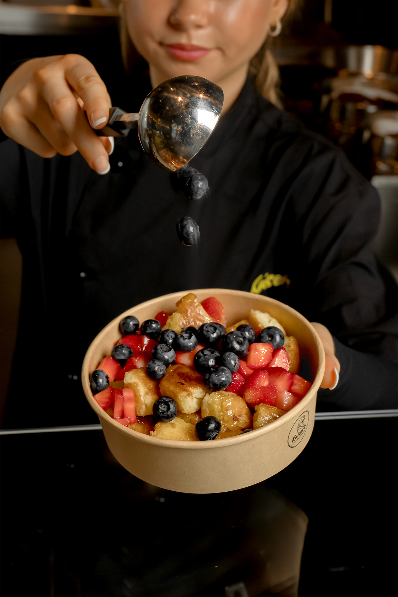 Kaiser's team member adding fresh blueberries to strawberry-blueberry Kaiser'schmarrn